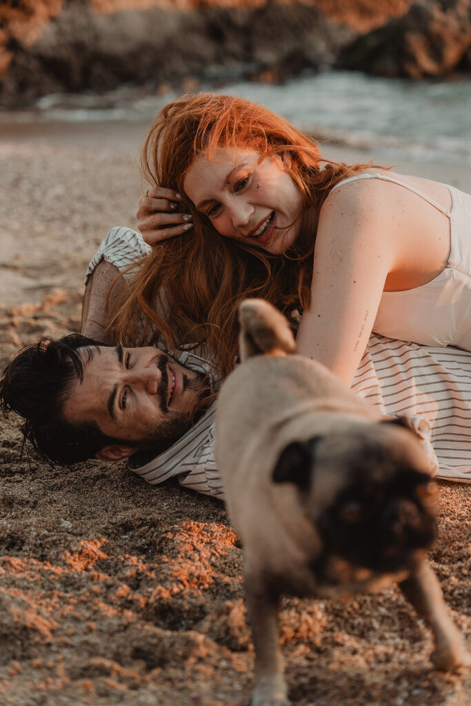 Sesión de pareja en Mazatlán de Xiomara y Alejandro junto al mar en la arena viendo a su perro