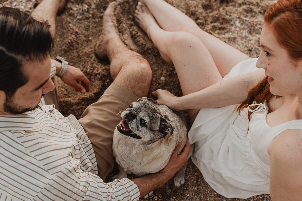 Sesión de pareja en Mazatlán de Xiomara y Alejandro junto al mar tocando a su pug con la boca abierta